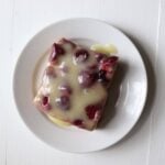 Raspberry biscuit pudding topped with vanilla cream glaze on a white plate.