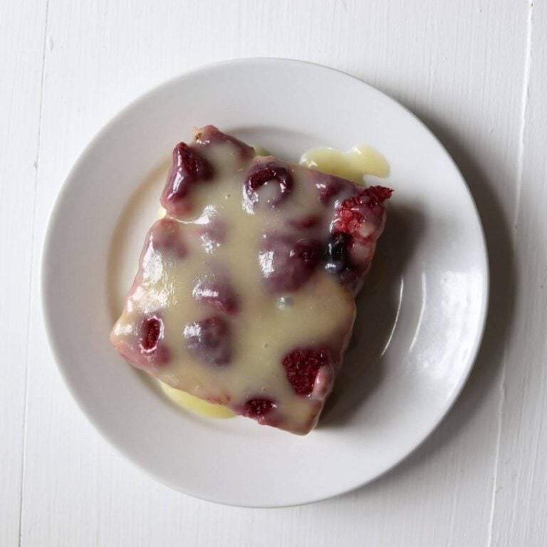 Raspberry biscuit pudding topped with vanilla cream glaze on a white plate.