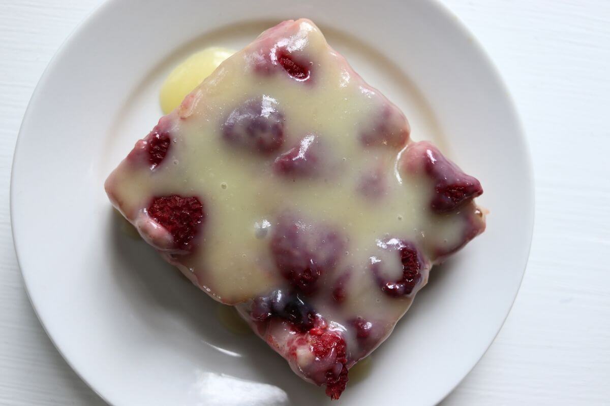 Square serving of raspberry biscuit pudding covered with cream glaze on a white plate.