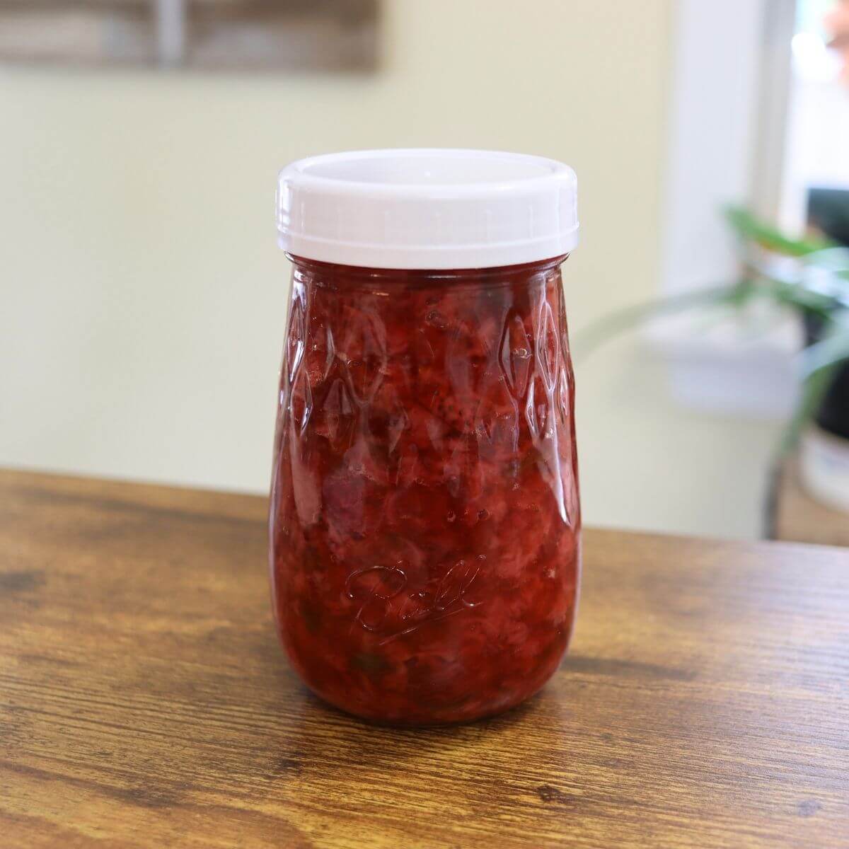 Jar of red fruit jam with a white lid on a table.