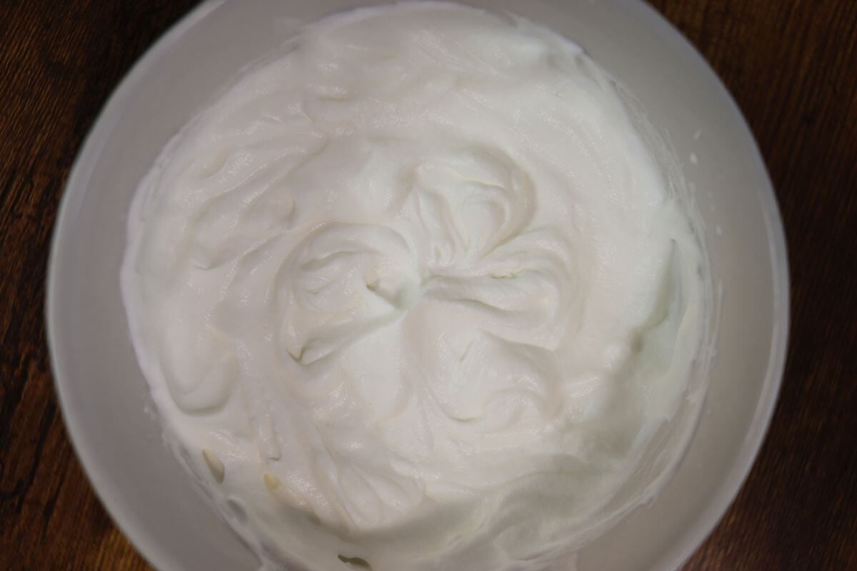 Whipped cream in a white bowl on a wooden table.