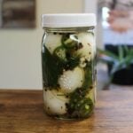 Jar of spicy pickled eggs with jalapeños, dill, and garlic on table.
