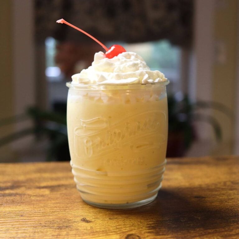 Tropical fruit milkshake topped with whipped cream and a maraschino cherry in a glass jar.