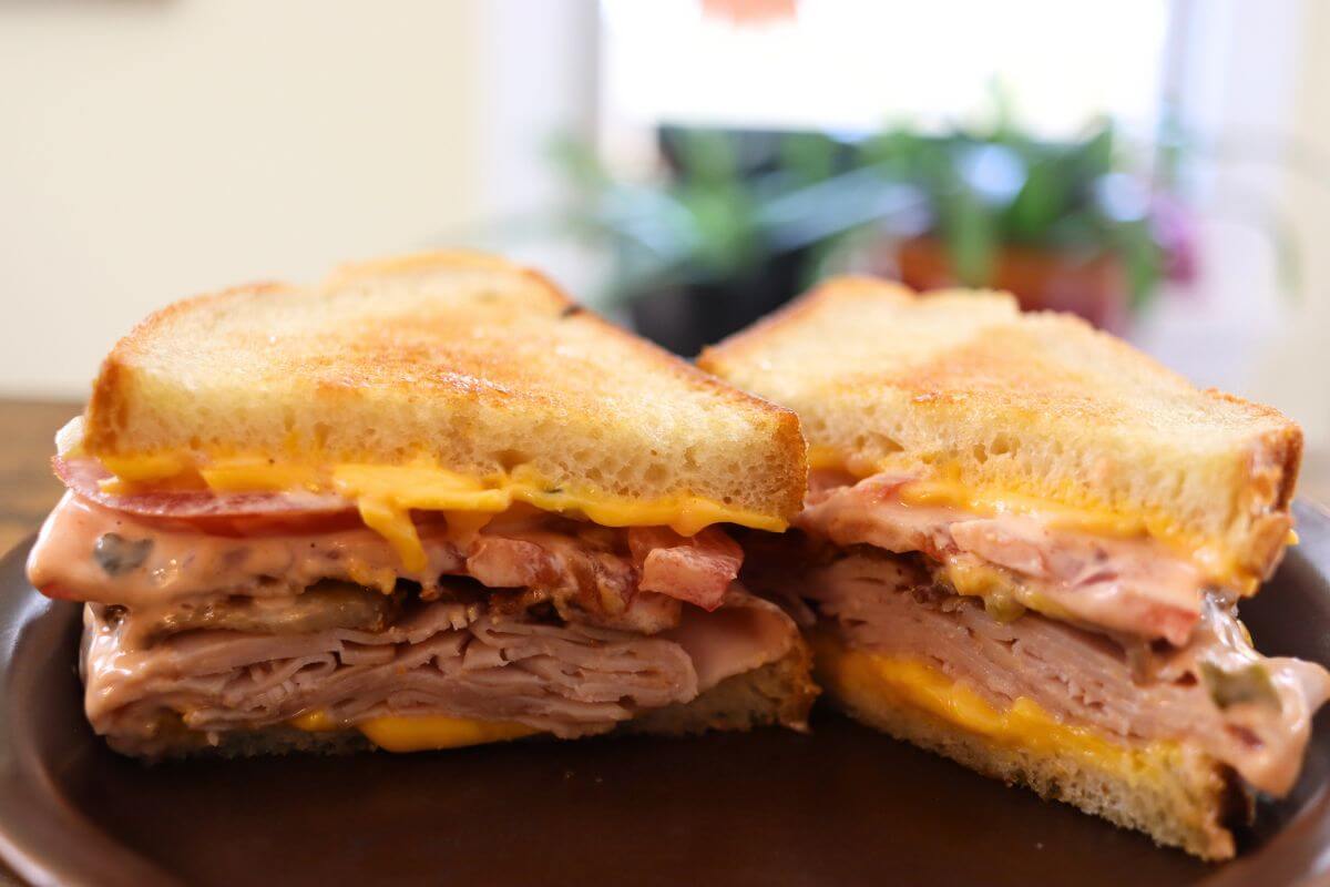Cut sandwich showing layers of turkey, bacon, cheese, and dressing.
