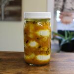 Yellow mustard pickled eggs in a mason jar with onions and spices.