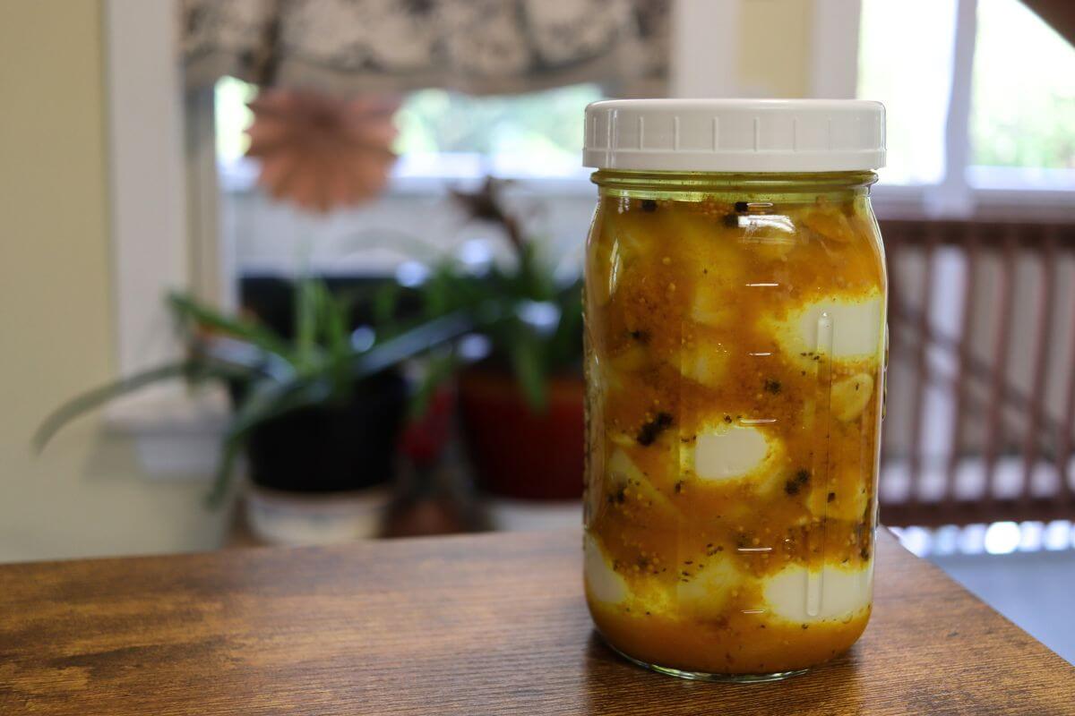 Jar of yellow mustard pickled eggs on a wooden tabletop.