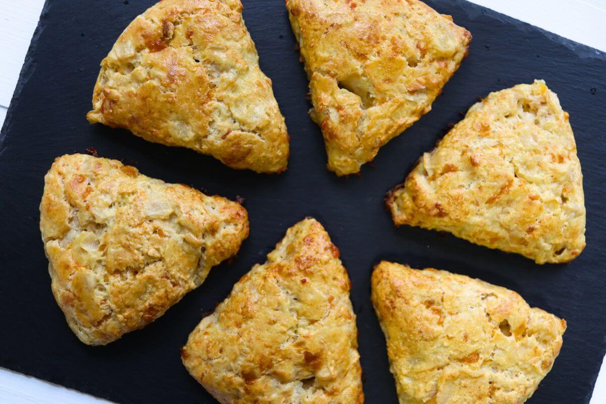 Homemade apple cheddar scones on a black slate board with visible apple pieces.