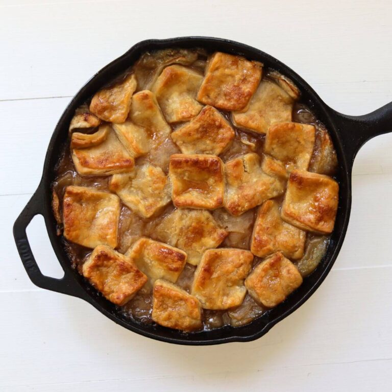 Cast iron skillet filled with apple pan dowdy topped with golden brown pastry squares over bubbling filling.