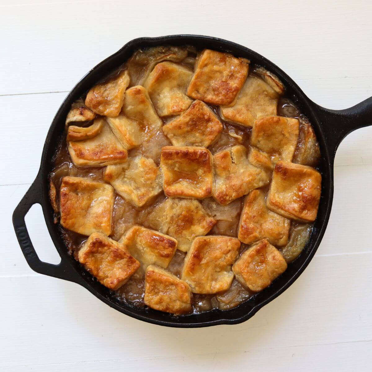 Cast iron skillet filled with apple pan dowdy topped with golden brown pastry squares over bubbling filling.