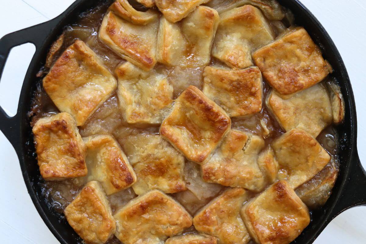Apple pan dowdy baked in a black cast iron skillet with browned pastry pieces over apple filling.