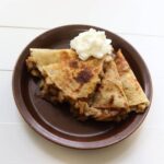 Apple pie quesadilla wedges with whipped cream on a brown plate.