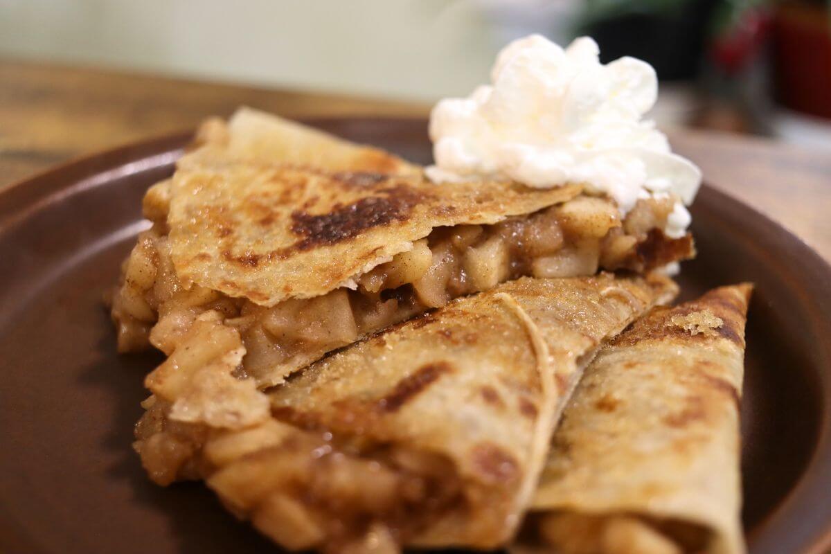 Quesadilla with homemade apple filling and whipped cream on a brown plate.