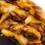 Stacked Cajun chicken quesadilla wedges with melted cheese on a dark board and the text "Cajun Chicken Quesadilla (crispy & cheesy)".