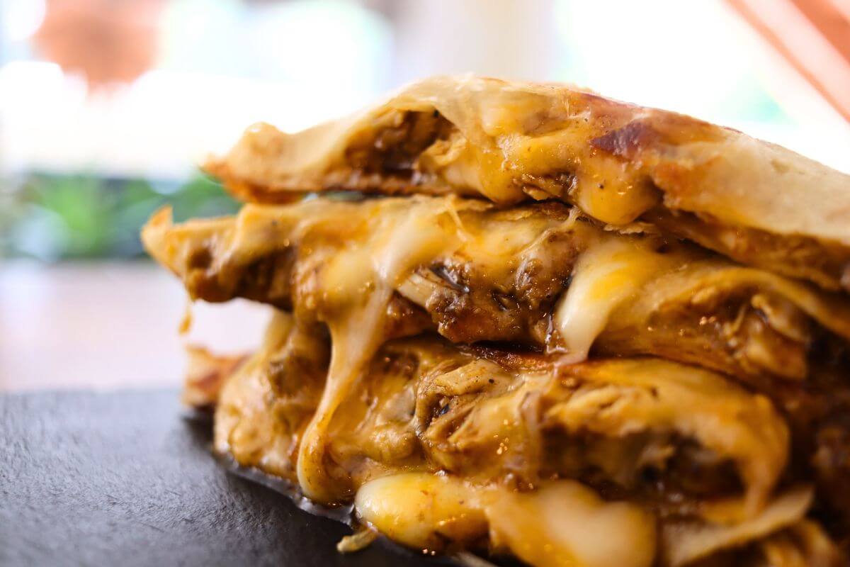 Melted cheese oozing from stacked Cajun chicken quesadilla wedges on a dark serving board.