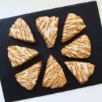 Cinnamon roll scones drizzled with vanilla glaze on a black slate board.