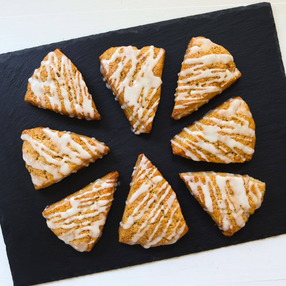 Cinnamon roll scones drizzled with vanilla glaze on a black slate board.