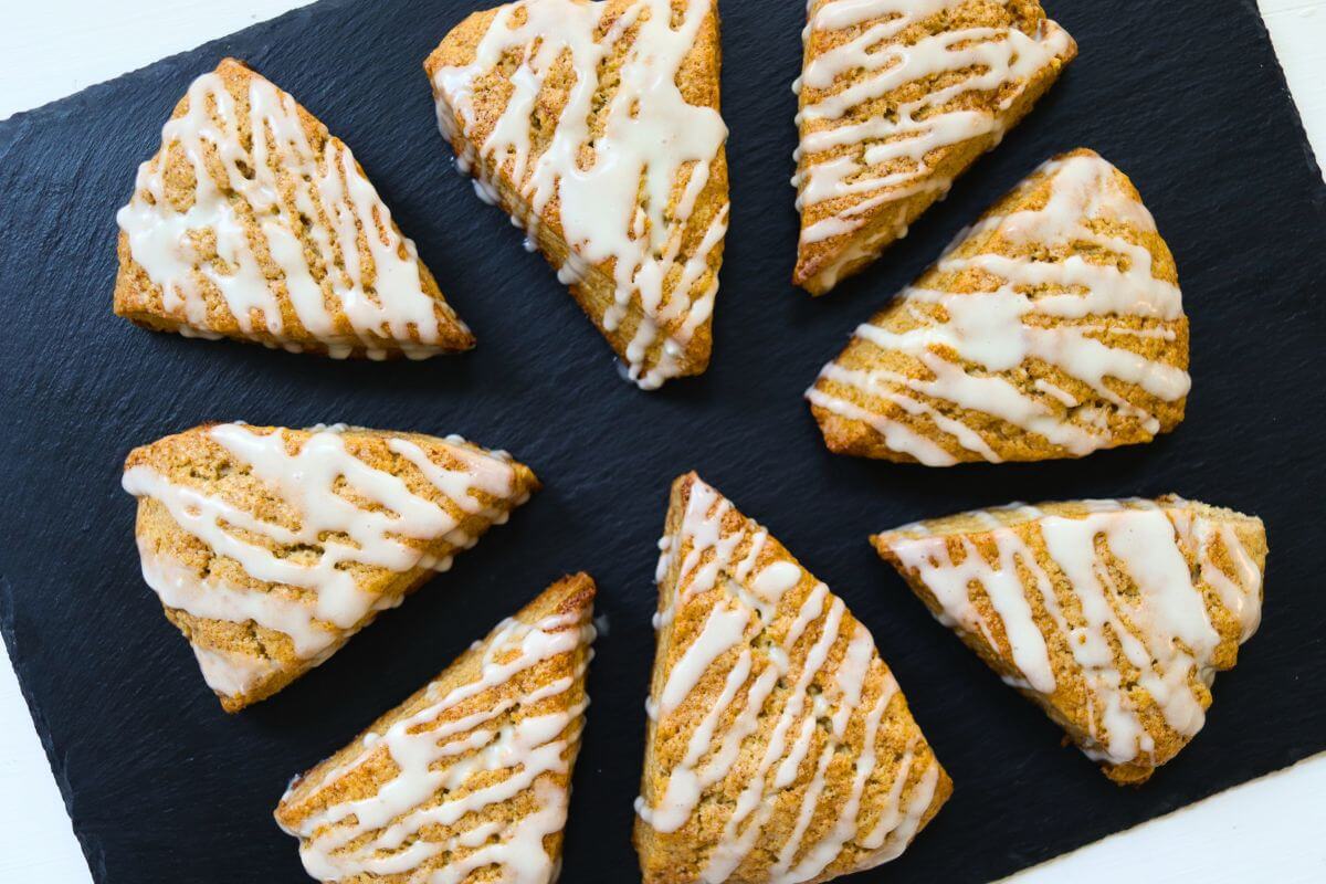 Eight glazed cinnamon roll scones arranged on a black slate serving board.