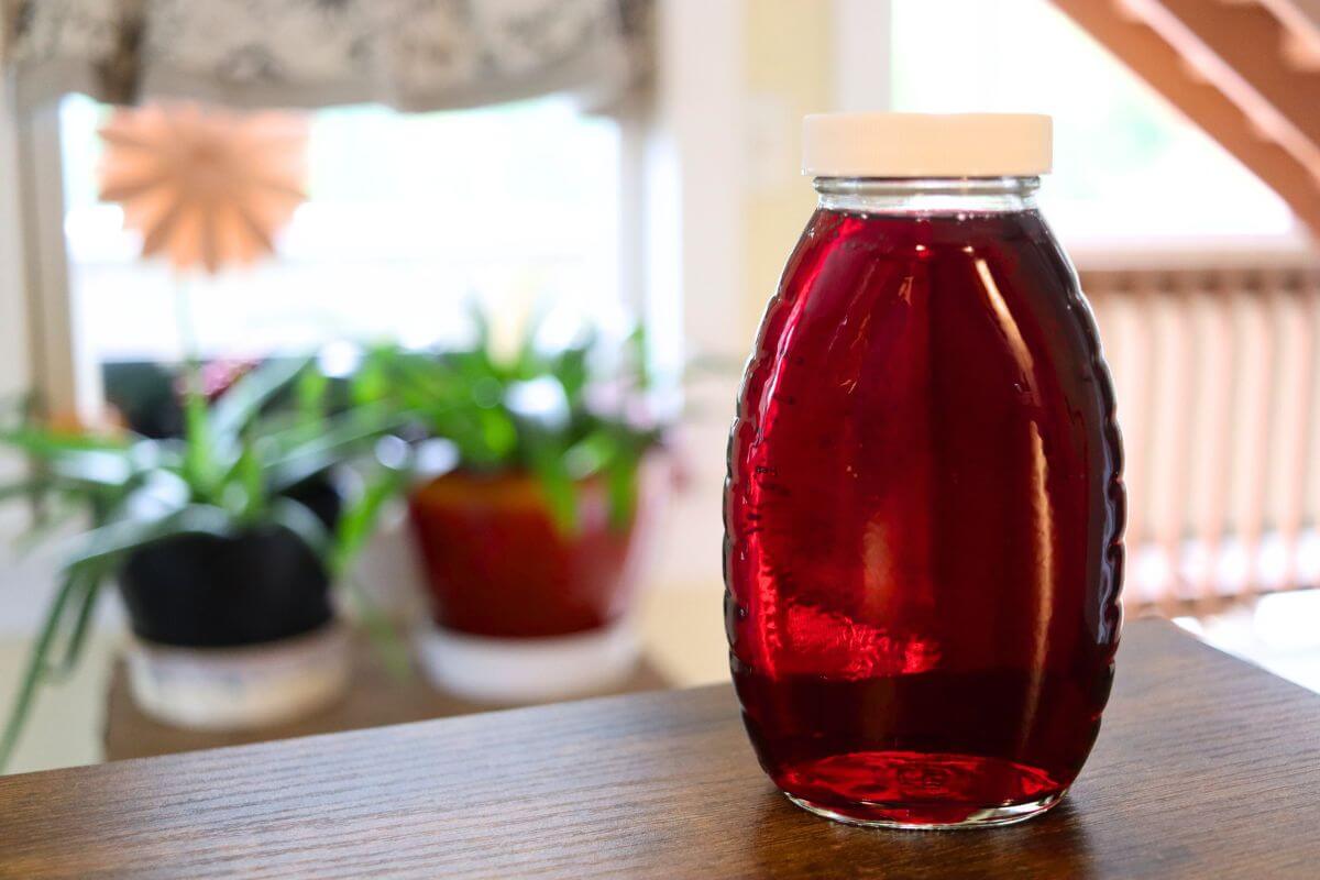 Clear glass bottle filled with homemade cranberry simple syrup on a wooden table with a blurred background.