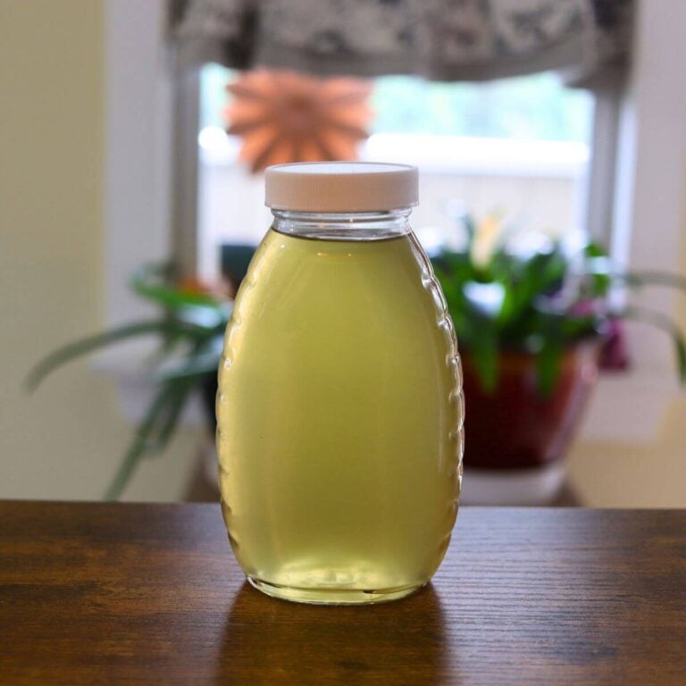 Homemade ginger simple syrup in a clear glass bottle with a white lid on a wooden table.