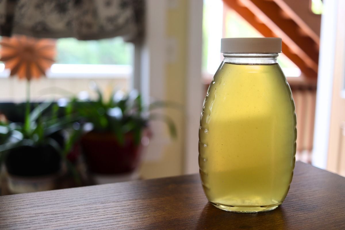 Bottle of homemade ginger simple syrup on a wooden tabletop with a softly blurred kitchen in the background.
