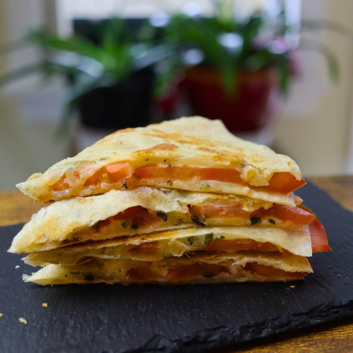 Grilled cheese and tomato quesadilla cut into wedges, showing melted cheese, tomato slices, and herbs.