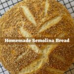 Round loaf of homemade semolina bread with a sesame seed topping on a wire cooling rack. Text reads "Homemade Semolina Bread".