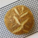 Homemade semolina bread topped with sesame seeds on a black wire cooling rack.