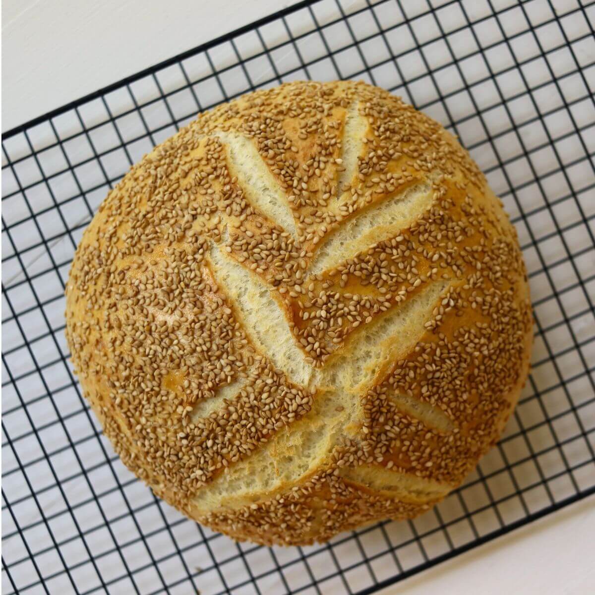 Homemade semolina bread topped with sesame seeds on a black wire cooling rack.