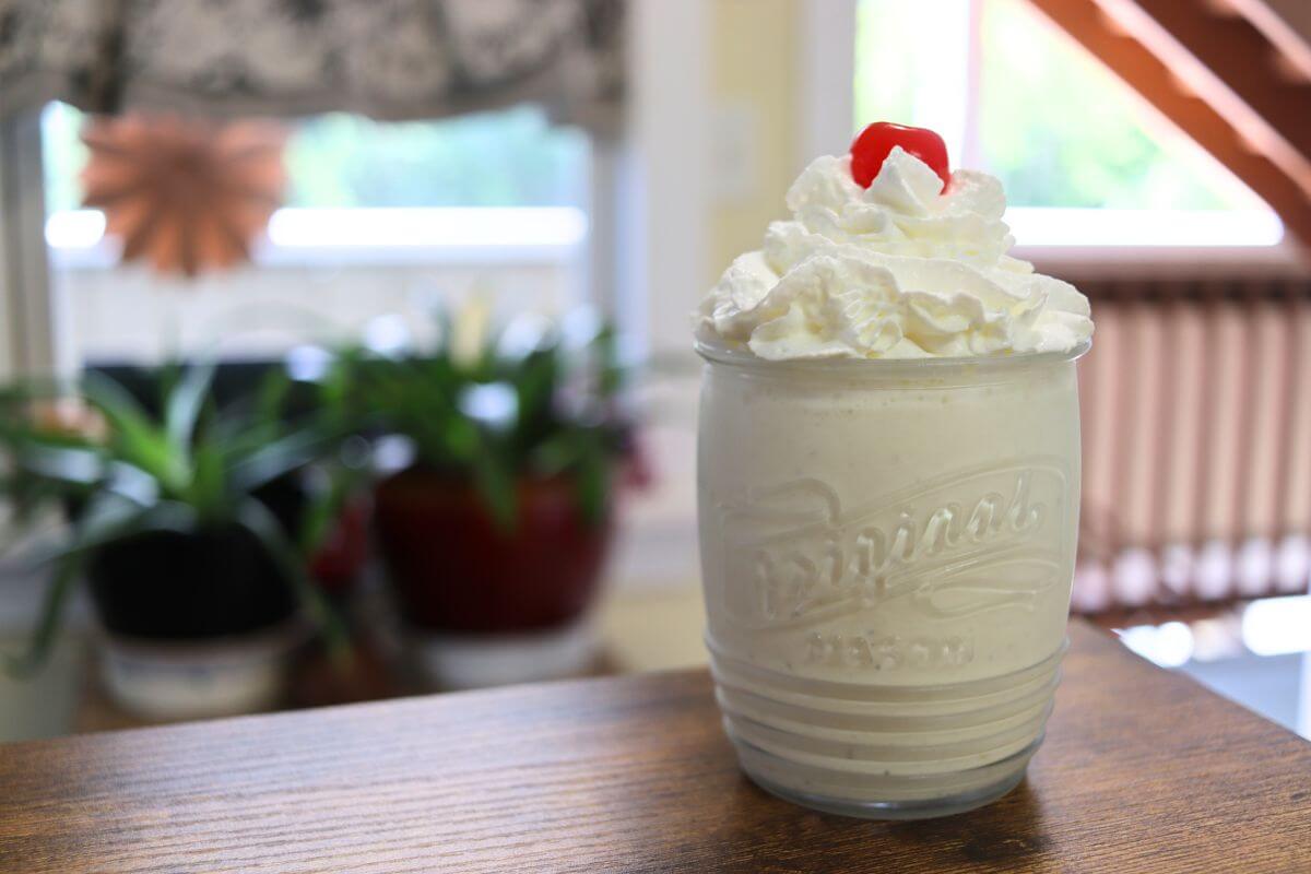Glass of malted milkshake topped with whipped cream and a maraschino cherry.