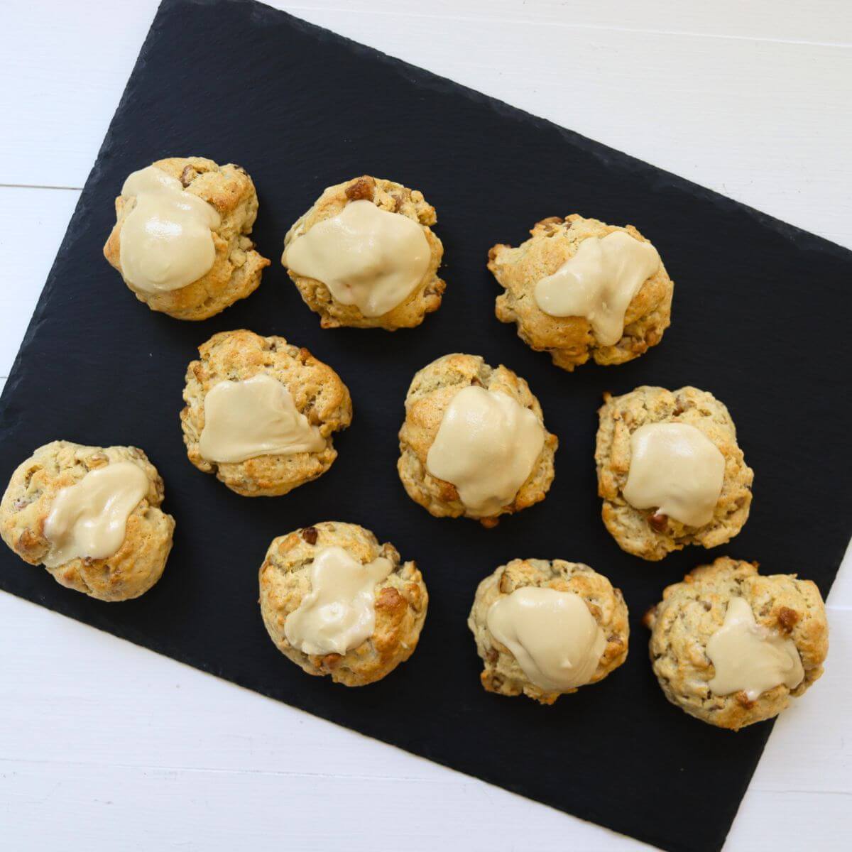 Maple walnut scones topped with maple icing arranged on a black serving board.