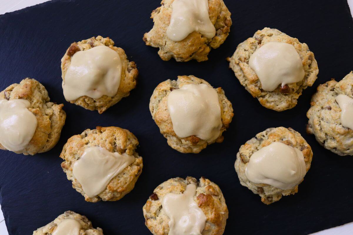 Homemade maple walnut scones with maple icing served on a black slate platter.
