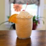 Orange creamsicle milkshake in a glass topped with whipped cream, a cherry, and an orange slice.