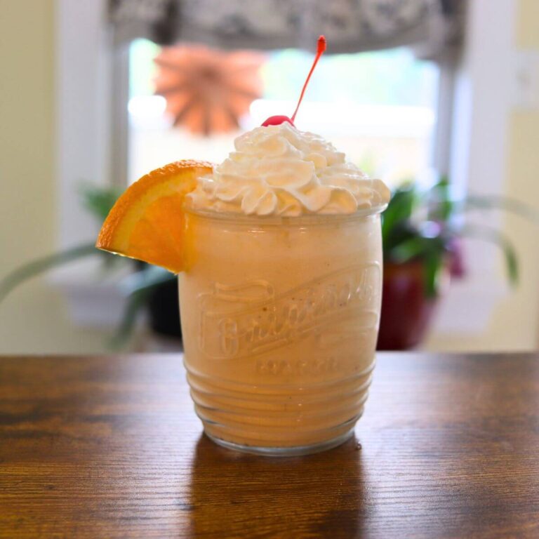 Orange creamsicle milkshake in a glass topped with whipped cream, a cherry, and an orange slice.