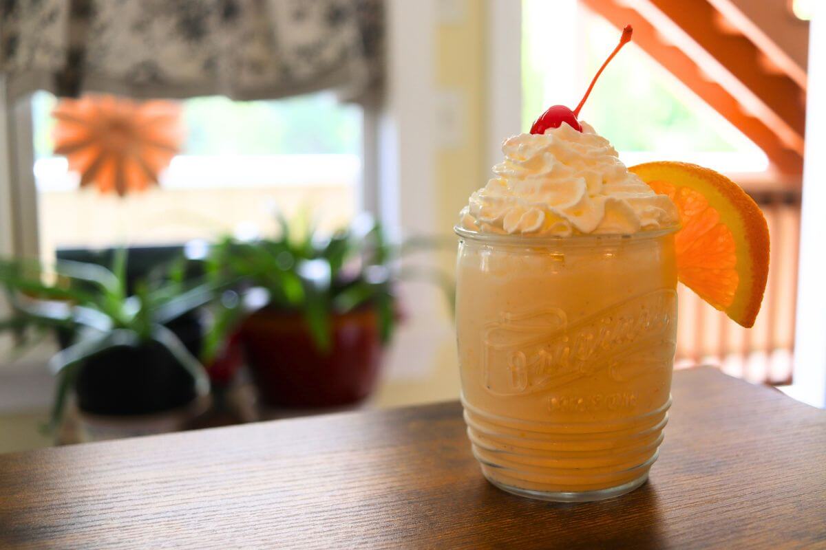 Glass of orange creamsicle milkshake topped with whipped cream, a cherry, and an orange slice.