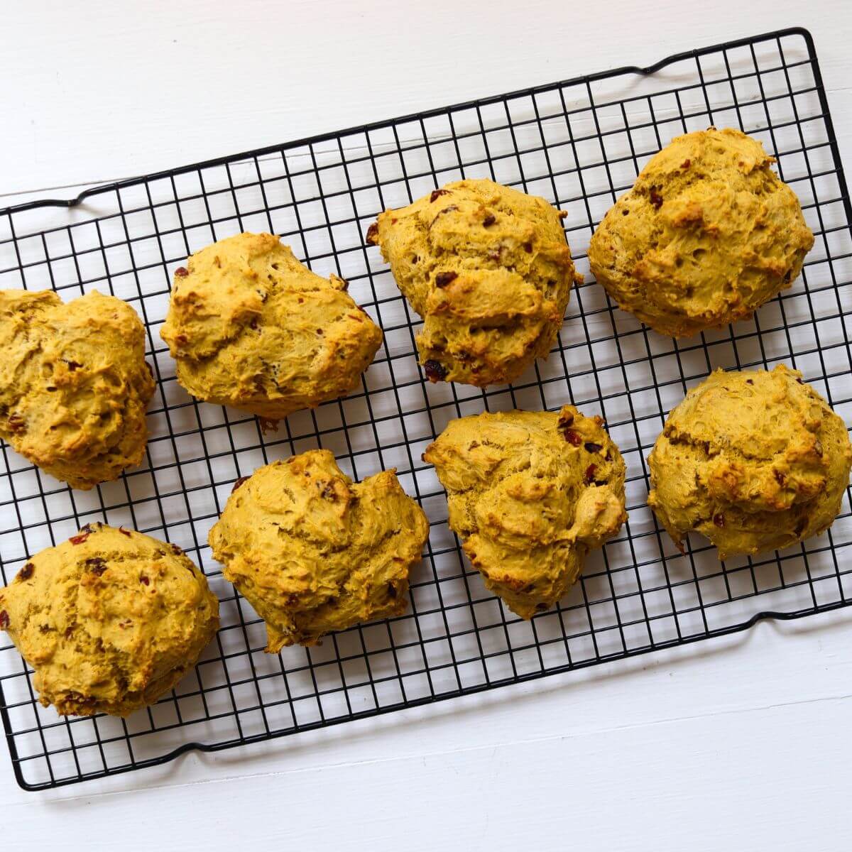 Eight pumpkin cranberry scones cooling on a black wire rack.