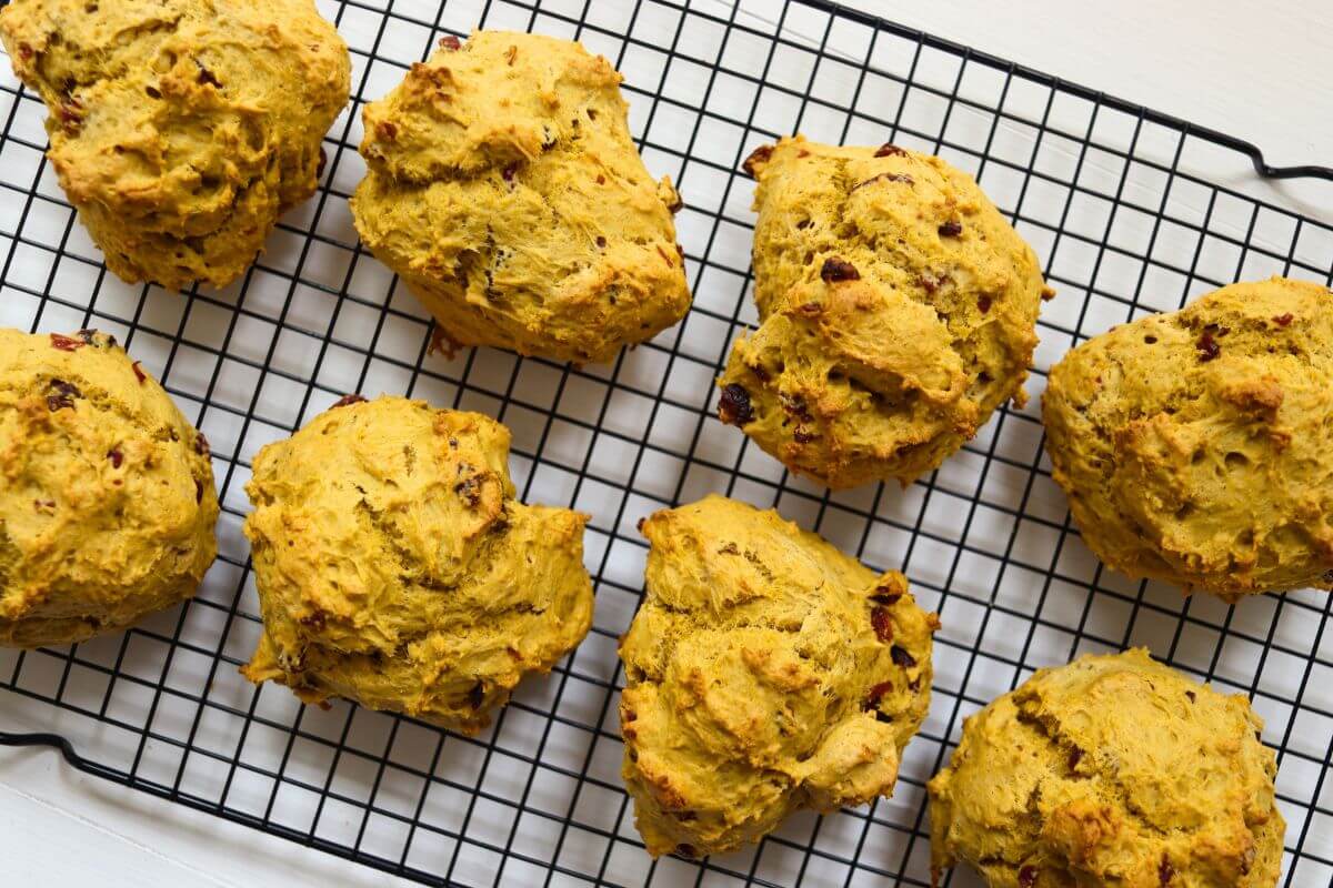 Freshly baked pumpkin cranberry scones arranged on a black cooling rack.