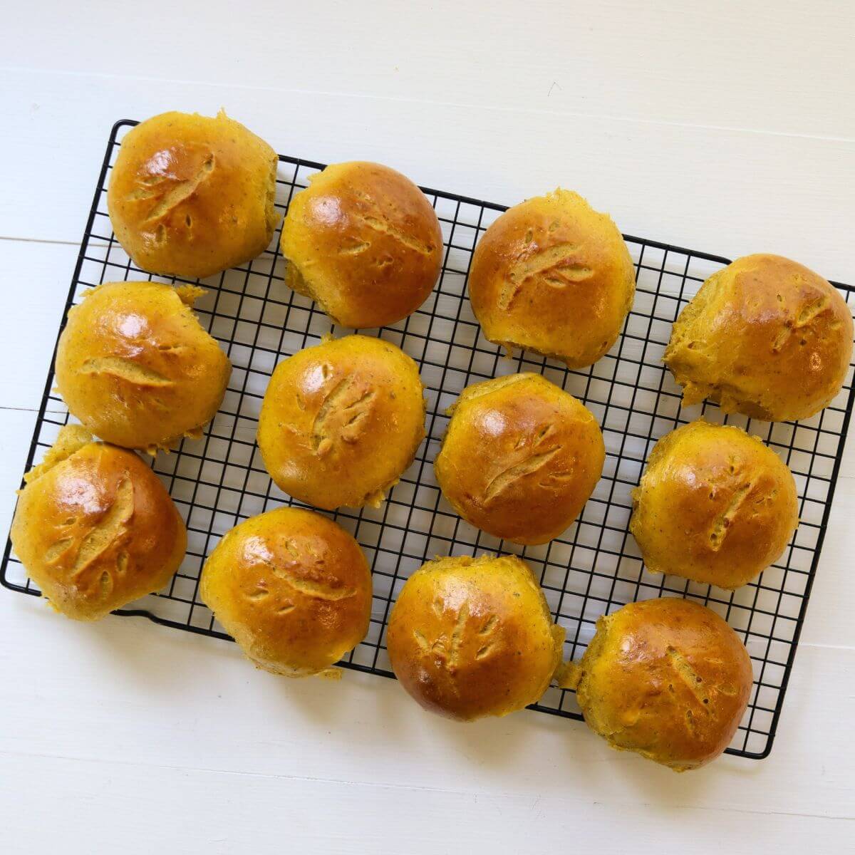 Golden brown savory pumpkin dinner rolls with scored tops arranged on a black cooling rack.