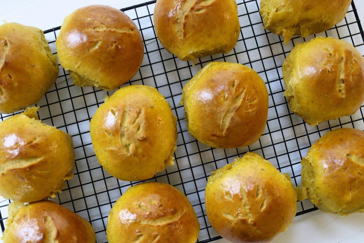 Savory pumpkin dinner rolls cooling on a wire rack with scored golden brown tops.