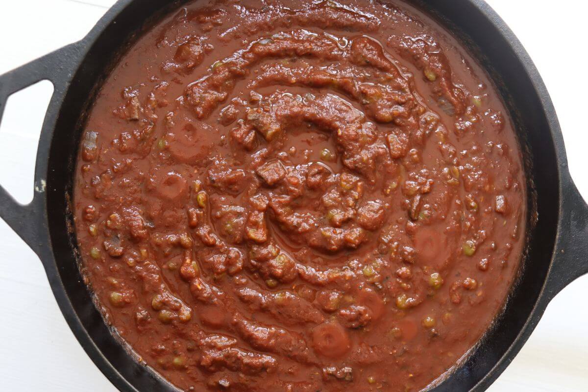 Black cast iron Dutch oven filled with thick tomato-based sauce.