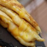 Stack of crispy three cheese quesadillas with gooey melted cheese on a black serving board. Text reads "Three Cheese Quesadilla".