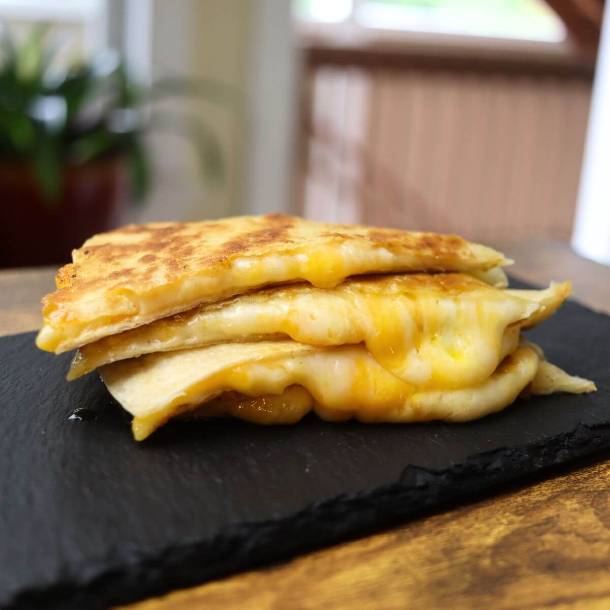 Stack of crispy three cheese quesadillas with melted cheese on a black serving board.