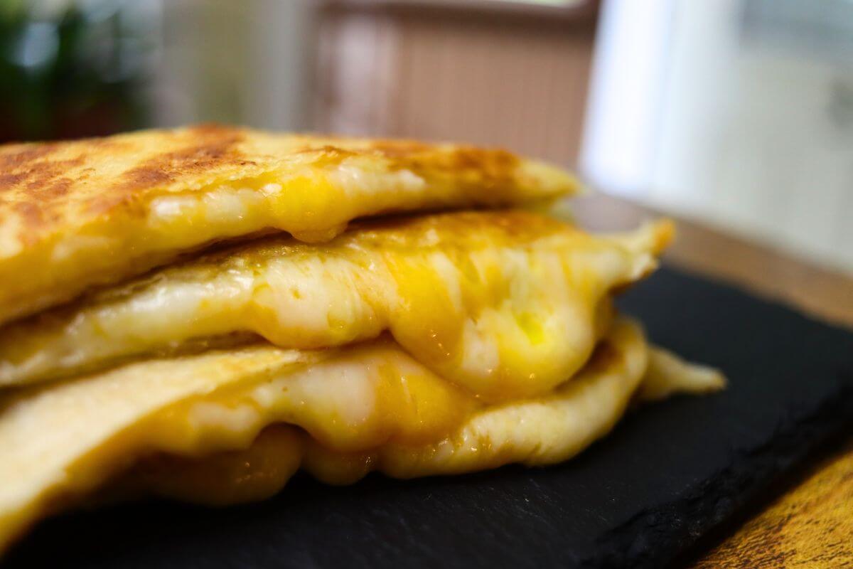Crispy three cheese quesadillas stacked on a black serving board with melted cheese visible.