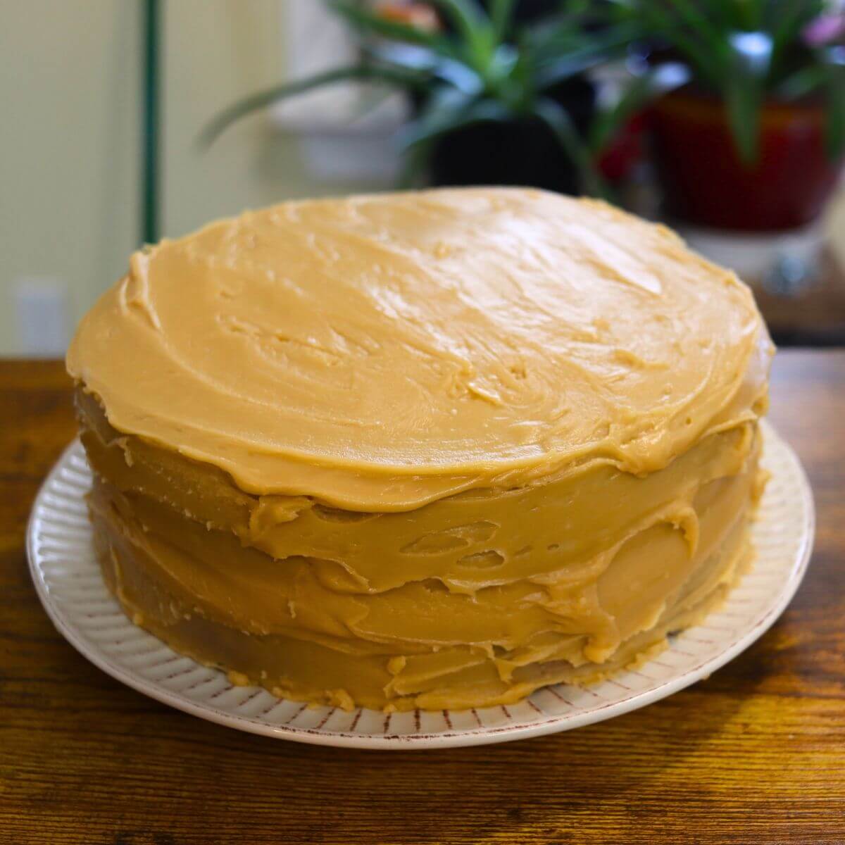 Vanilla caramel cake frosted with homemade caramel frosting on a white cake plate.