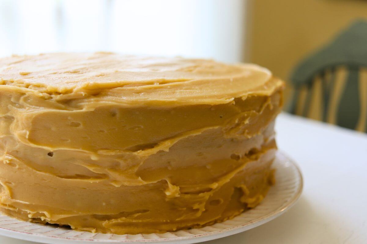 Homemade vanilla caramel cake covered with caramel frosting on a white serving plate.