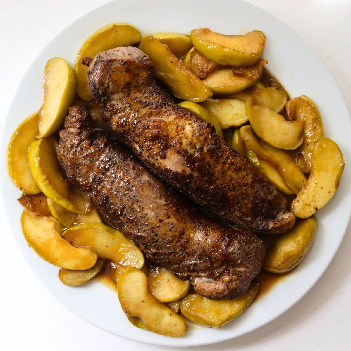 Apple and pork tenderloin with cooked apple slices and maple Dijon sauce on a serving platter.