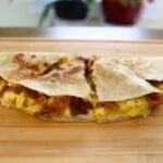 Bacon egg and cheese quesadilla wedges filled with scrambled eggs, crispy bacon, and melted cheese.