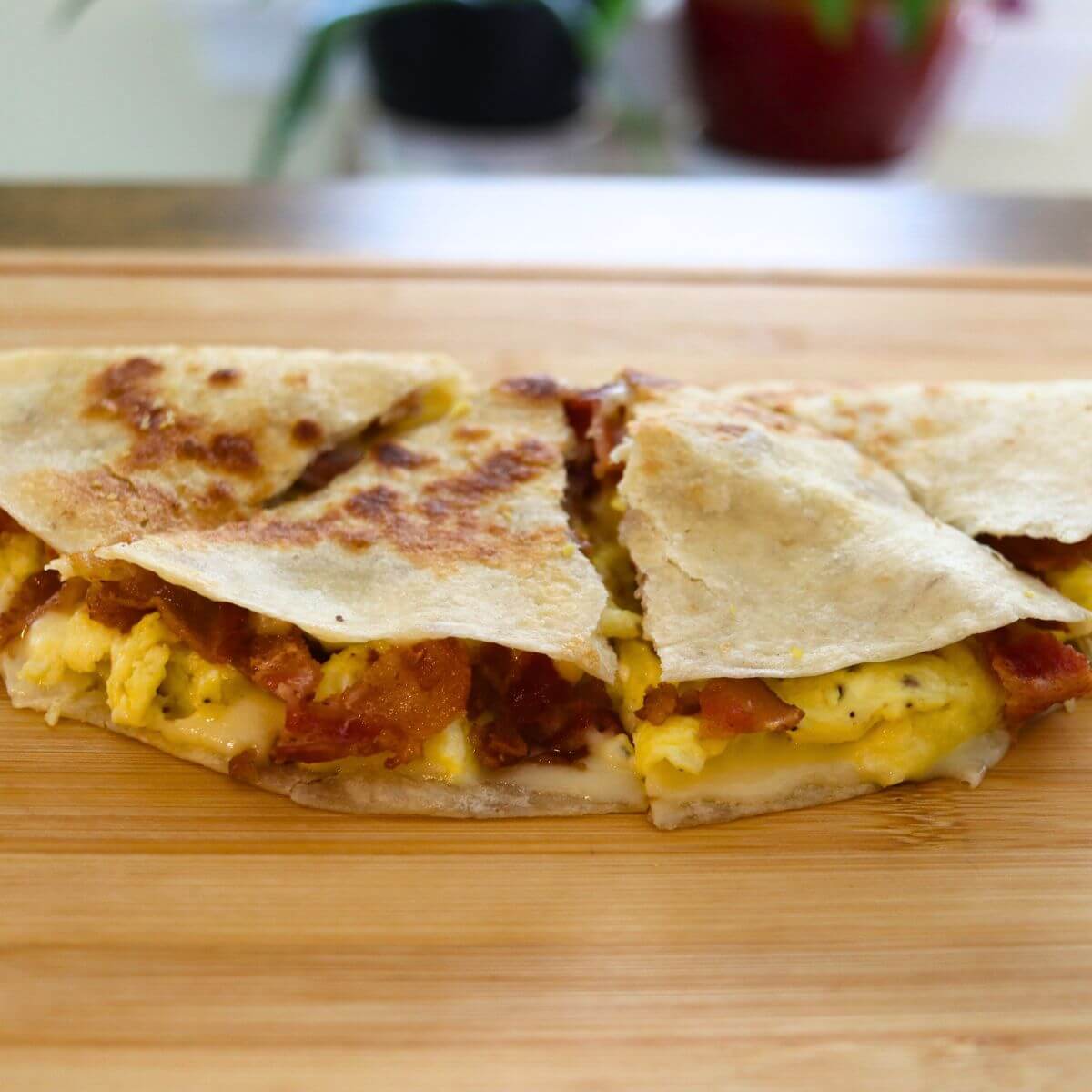 Bacon egg and cheese quesadilla wedges filled with scrambled eggs, crispy bacon, and melted cheese.