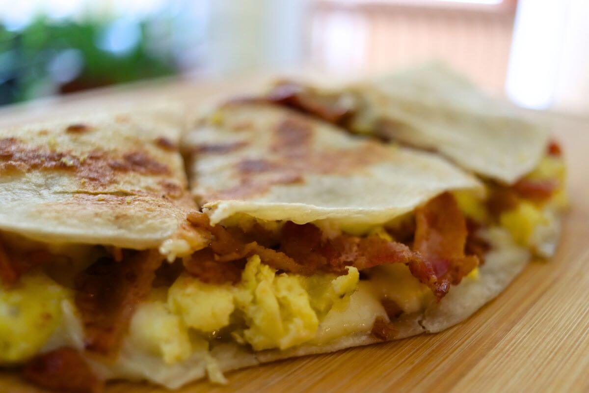 Golden pan-fried bacon egg and cheese quesadilla cut into wedges on a wooden cutting board.
