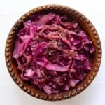 Braised red cabbage with pieces of cooked apple and onion served in a wooden bowl.