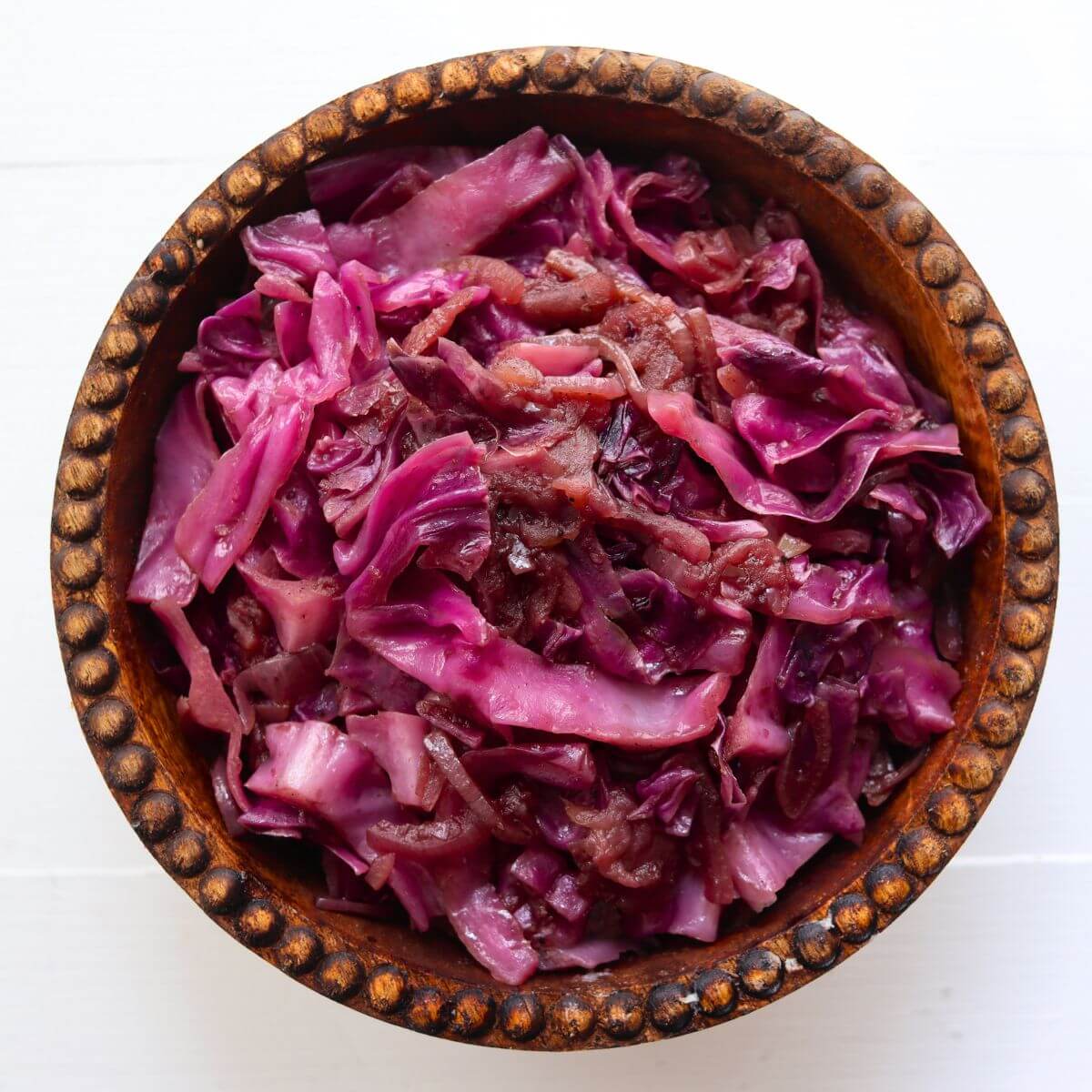 Braised red cabbage with pieces of cooked apple and onion served in a wooden bowl.